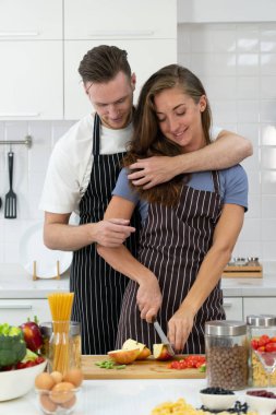 Kocası mutfakta ona sarılırken sağlıklı salata yapmak için sebze doğrayan genç bir kadın. çift kavramı