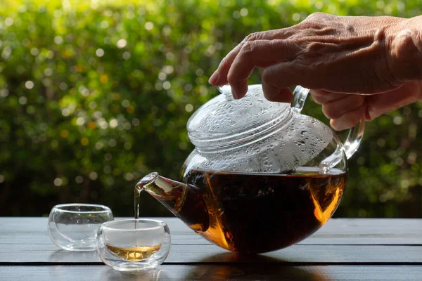 picture of people pouring chinese tea from galss kettle  into cup to make afternoon tea in garden