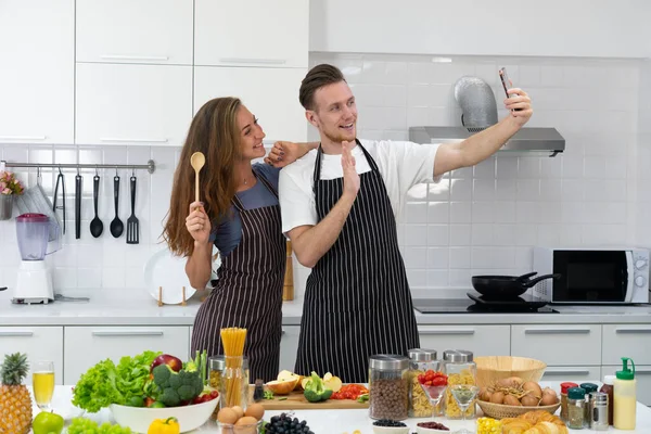 年轻的高加索夫妇在家里厨房做健康早餐的时候用智能手机自拍 — 图库照片