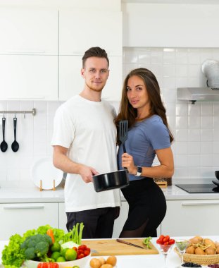 Genç beyaz bir çift mutfak malzemelerini ellerinde tutuyorlar ve kahvaltı hazırlamak için mutfakta duruyorlar. aile kavramı