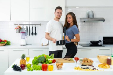 Genç beyaz bir çift mutfak malzemelerini ellerinde tutuyorlar ve kahvaltı hazırlamak için mutfakta duruyorlar. aile kavramı