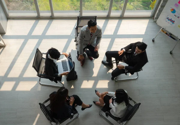 view from above of international business team including caucasian and asian people standing near window in office and discussing about project. diversity in business concept