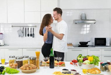 Genç, mutlu beyaz çift yıldönümü buluşmasında mutfakta yavaş yavaş dans ediyorlar.