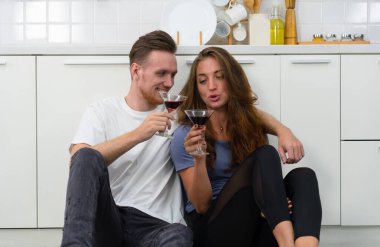 Genç, beyaz bir çiftin yıl dönümünde mutfakta oturup şarap içerken çekilmiş otantik bir fotoğrafı.