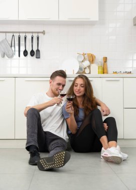 Genç, beyaz bir çiftin yıl dönümünde mutfakta oturup şarap içerken çekilmiş otantik bir fotoğrafı.