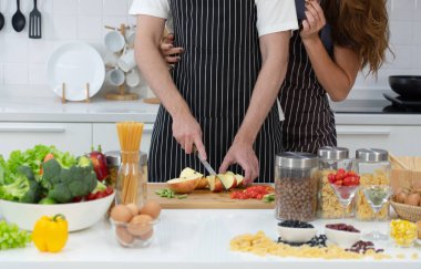 Kahvaltıda organik sağlıklı salata pişirmek için elma doğrayan genç beyaz bir adam. Bu arada arkadaşı mutfakta ona sarılıyor.