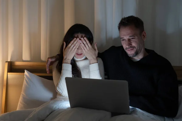 cuacasian couple watcing scary movies from streming program in computer together on bed at home in the night