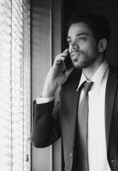 portrait of young businessman looking out of window and using smartphone to talk with client. business concept (black and white monochrome)