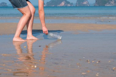 Genç Asyalı kadın çevreyi ve deniz ekosistemini korumak için plajdan kullanılmış plastik şişe topluyor.
