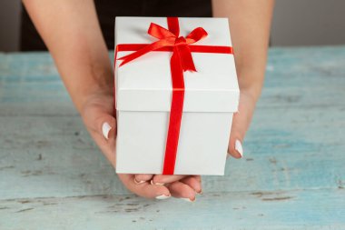 Mavi arka planda beyaz hediye kutusu tutan kadın.