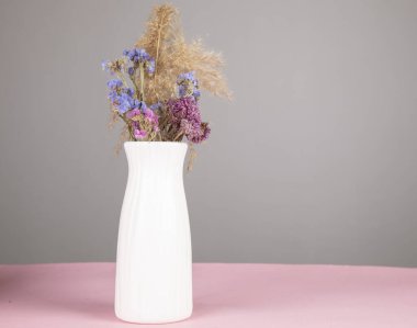 Pembe masa arkasındaki vazoda kurumuş çiçekler.