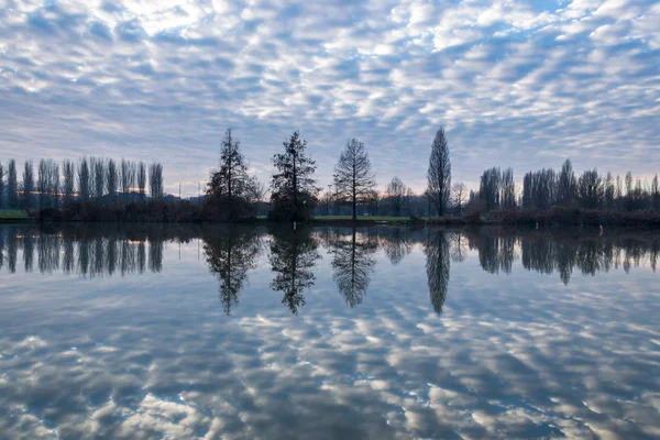 Puesta de sol de invierno en la orilla de un lago con nubes reflejadas en th —  Fotos de Stock