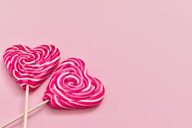 Pembe arka planda iki parlak lolipopun üzerinde, tahta bir sopanın üzerinde beyaz bir kurdeleyle duran bir kalp. Tebrik kartı. Yukarıdan manzara. Düz plan. Minimalizm.