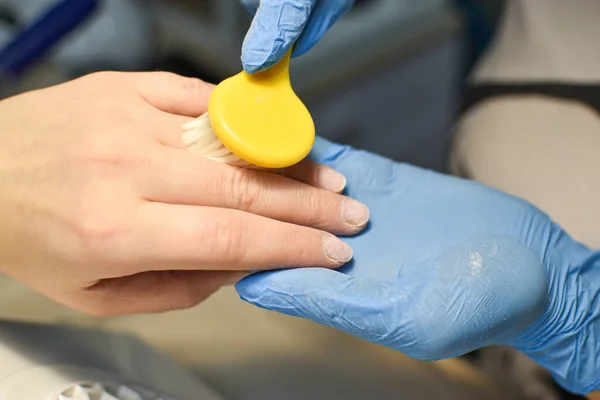 The manicure master holds a yellow brush in his hand. Preparation for manicure and pedicure.