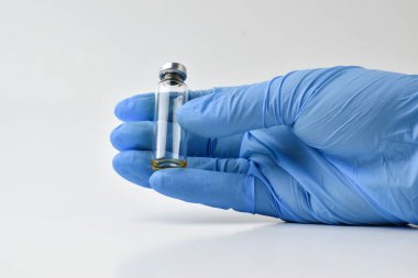 Mavi eldivenli bir el beyaz bir aşı şişesini izole eder. Boşluğu kopyala.