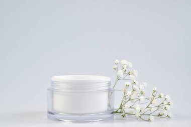 Boş bir kavanoz ve krema, maske ve fırça için çiçekler. Beyaz arka planda bir kavanoz krema. Doğal kozmetik ürünleri ve parfümler. Spa tedavileri. Markalaşma ve ürün sunumu için bir yer.