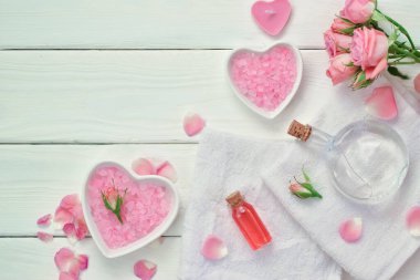 Pembe arka planda gül ve çeşitli kozmetik şişeleri ve pamuk havlular. Spa planlayıcısı. Diyet vücut bakımı. Flatt lay. Üst görünüm.
