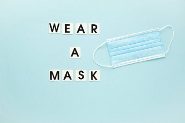 Tıbbi maske ve kısa mesaj açık mavi arka planda bir maske takın. Poster, pankart virüs koruması. Boş bir alan.