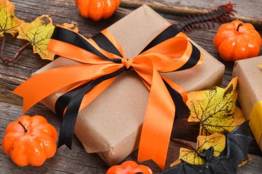 Cadılar Bayramı için turuncu kurdeleli hediye kutusunun yakın çekimi. Cadılar Bayramı için balkabakları ve hediyelerle dolu ahşap bir arka planda neşeli bir kompozisyon. Üst Manzara. Boşluğu kopyala