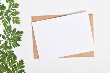 Davetiye şablonu üzerinde yeşil dalları olan beyaz bir zarf ile birlikte. Düz düzen, üst görünüm, kopyalanacak bir yer.