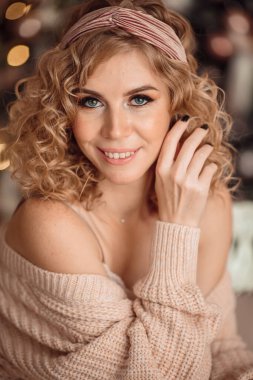 Hoş bir sarışının portresi. Kıvırcık saçlı, rahat ev kıyafetleri içinde. Noel ağacında kutlama yapıyor..