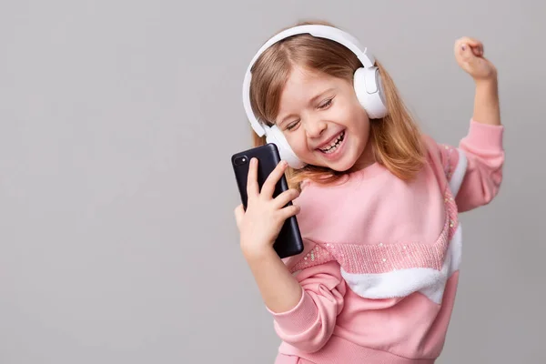 A little girl blogger influencer records a blog video on a smartphone, dances and listens to music with headphones on a yellow isolated background. — Stock Photo, Image