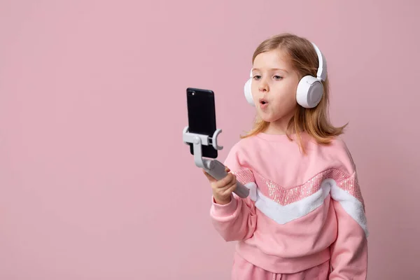 Mała blondynka blogerka słucha muzyki z białymi słuchawkami, uczy się języka lub powtarza lekcję, uczy się na odległość na odosobnionym tle. — Zdjęcie stockowe