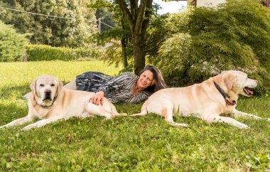 Bahçedeki çimlerin üzerinde iki Labrador köpeği olan mutlu olgun bir kadın..
