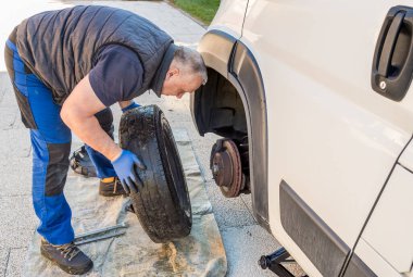 Rutin araç bakım prosedürü sırasında bir minibüse tekerlek takan bir adam..