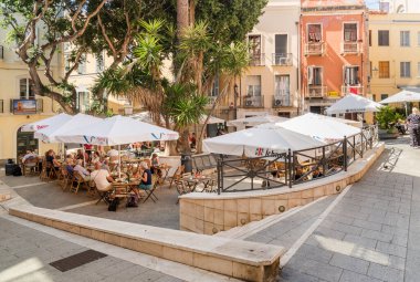 Cagliari, Sardinya, İtalya - 4 Ekim 2025: Cagliari 'nin canlı bir meydanındaki açık hava bar ve dükkanlarının yer aldığı şehir manzarası. Şehir hayatı, eğlence ve Akdeniz atmosferi.