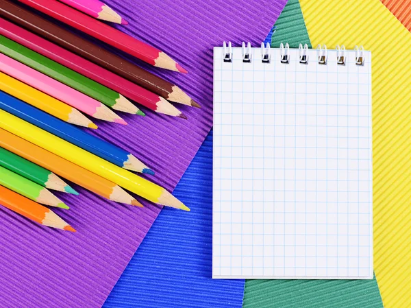 Lápices de color sobre papel con cuaderno — Foto de Stock