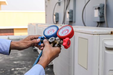 Manifold göstergesi kullanan hava tamircisi, endüstriyel fabrika klimalarını temizleme ve açık hava kompresör ünitesini kontrol ettikten sonra doldurmak için ekipman ölçüyor..