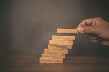 Yakın çekim el, çöküşü veya finansal risk yönetimi ve stratejik planlama kavramlarını önlemek için merdivenlere dizilmiş odun blok kulesi veya jenga oyunu veya merdiven yerleştirmektir.