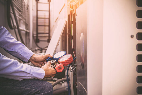Air repairman technician using manifold gauge is measuring equipment for filling industrial factory air conditioners after cleaning and checking for maintenance outdoor air compressor unit.