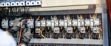 Elektrik mühendisinin ölçüm ekipmanlarını kullanarak devre kesici ve kablo tesisat sistemindeki elektrik akımını kontrol ederek ana güç dağıtım panosunun bakımı için yakın çekim eli..