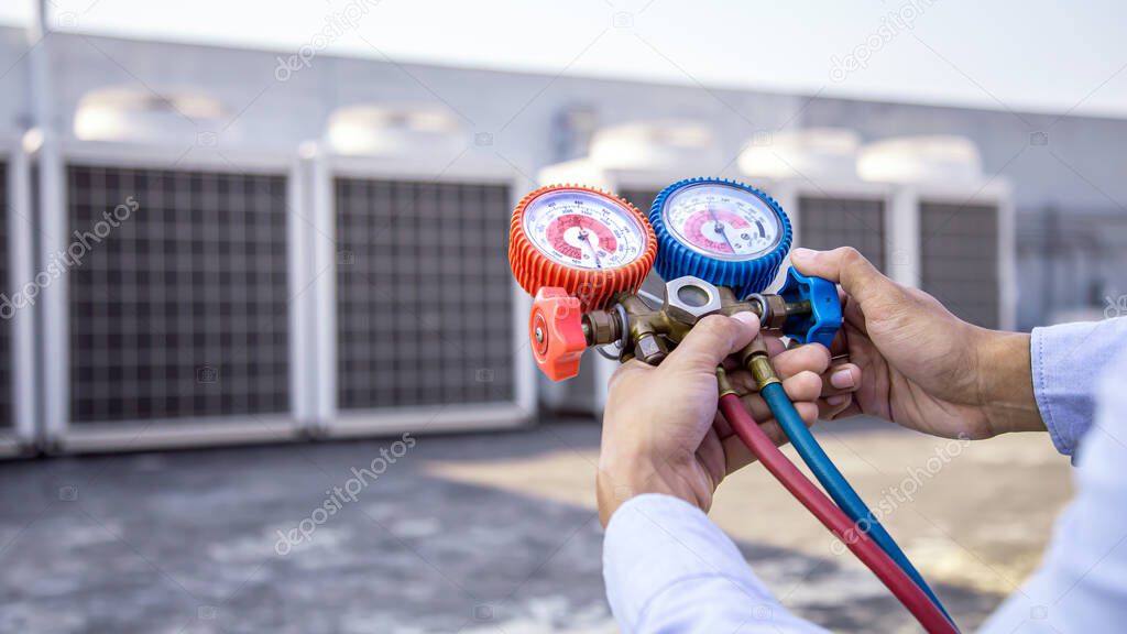Close up hand of air repairman using manifold gauge is measuring equipment for checking refrigerant and filling industrial factory air conditioners after cleaning and maintenance outdoor air compressor unit.