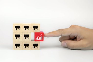 Yakın plan el, bayilik mağazası simgesiyle istiflenmiş küp tahta oyuncak blokları üzerindeki grafik simgesini seçiyor. İş büyümesi ve finansal pazarlama planlaması için.