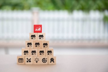 Yakından bakıldığında, piramit şeklinde ve bayilik mağazası ikonu ile istiflenmiş küp tahta oyuncak blokları seçiyor. Ticari büyüme ve finansal pazarlama planlamasının genişleme stratejisi için.