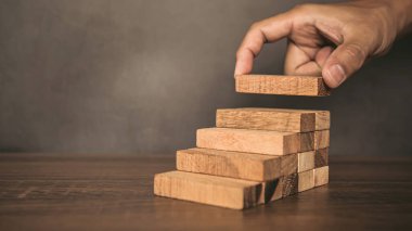 Yakın plan el, çöküşü veya finansal risk yönetimi ve stratejik planlama kavramlarını önlemek için piramit şeklinde dizilmiş ahşap blok kulesini ihtiyatlı bir şekilde yerleştiriyor.