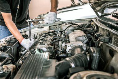 Otomobil tamircisinin yakın çekimli elleri araba tamirhanesinde tamir ve bakım için ingiliz anahtarını kullanıyor. Araç bakımı kontrolü ve sabit ve hizmet sigortası kavramları.