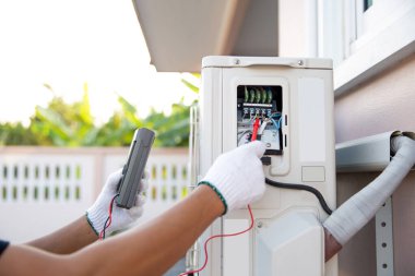 Kurulum ve havalandırma hizmetleri bakımından sonra açık hava kompresör ünitesindeki devre kesicideki elektrik akımını kontrol etmek için ölçüm ekipmanı kullanan teknisyenlerin ellerini kapat