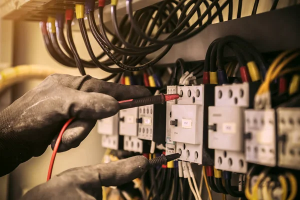 Elektrik mühendisinin ölçüm ekipmanlarını kullanarak devre kesici ve kablo tesisat sistemindeki elektrik akımını kontrol ederek ana güç dağıtım panosunun bakımı için yakın çekim eli..