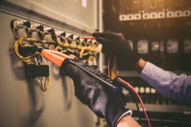 Elektrik mühendisinin ölçüm ekipmanlarını kullanarak devre kesici ve kablo tesisat sistemindeki elektrik akımını kontrol ederek ana güç dağıtım panosunun bakımı için yakın çekim eli..