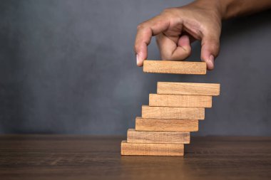 Yakın plan el, çöküşü veya finansal risk yönetimi ve stratejik planlama kavramlarını önlemek için piramit şeklinde dizilmiş ahşap blok kulesini ihtiyatlı bir şekilde yerleştiriyor.