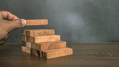 Yakın plan el, çöküşü veya finansal risk yönetimi ve stratejik planlama kavramlarını önlemek için piramit şeklinde dizilmiş ahşap blok kulesini ihtiyatlı bir şekilde yerleştiriyor.