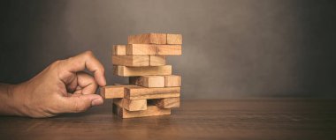 Yakın plan el, diğer ahşap bloklardan tahta blokları söküp kule şeklinde finansal risk yönetimi ve stratejik planlama kavramlarına yerleştirdi..