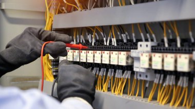 Elektrik mühendisinin ölçüm ekipmanlarını kullanarak devre kesici ve kablo tesisat sistemindeki elektrik akımını kontrol ederek ana güç dağıtım panosunun bakımı için yakın çekim eli..