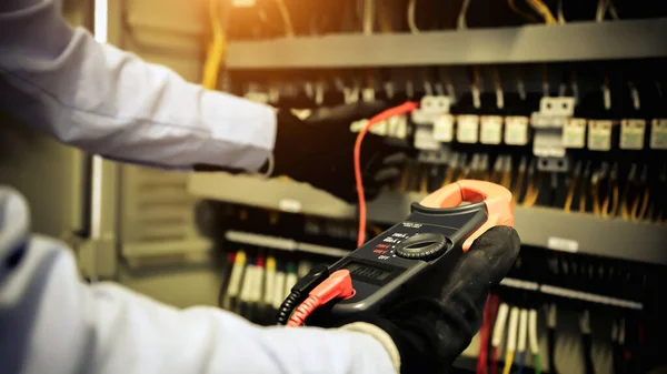 Elektrik mühendisinin ölçüm ekipmanlarını kullanarak devre kesici ve kablo tesisat sistemindeki elektrik akımını kontrol ederek ana güç dağıtım panosunun bakımı için yakın çekim eli..