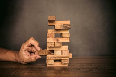 Yakın plan el, diğer ahşap bloklardan tahta blokları söküp kule şeklinde finansal risk yönetimi ve stratejik planlama kavramlarına yerleştirdi..