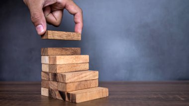 Yakın plan el, çöküşü veya finansal risk yönetimi ve stratejik planlama kavramlarını önlemek için piramit şeklinde dizilmiş ahşap blok kulesini ihtiyatlı bir şekilde yerleştiriyor.